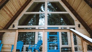 A cabin with a wooden exterior, a balcony with blue chairs, and a stack of firewood at the base. - Salted Roots Blue Door A-Frame Cabin (Seward)