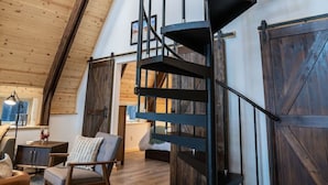 A spacious loft with a high ceiling, a spiral staircase, and a rustic wooden interior. - Salted Roots Blue Door A-Frame Cabin (Seward)