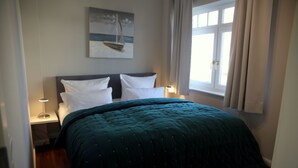 Ein ordentlich bezogenes Bett mit einer dunkelblauen Steude, zwei weißen Kissen und einem an der Wand hängenden Gemälde eines Segelboots.