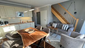 Eine moderne Küche mit weißen Schränken, einem Holztisch und einem grauen Sofa.