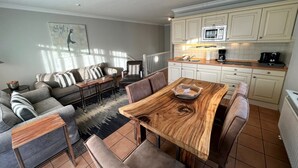 Ein modernes Wohnzimmer mit Esstisch, Sofas und einer Küchenzeile mit Schränken und Geräten.