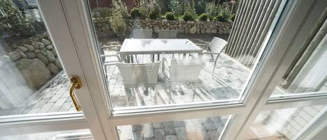 A glass door leading to an outdoor patio with a table and chairs, a stone wall, and a view of a residential area.