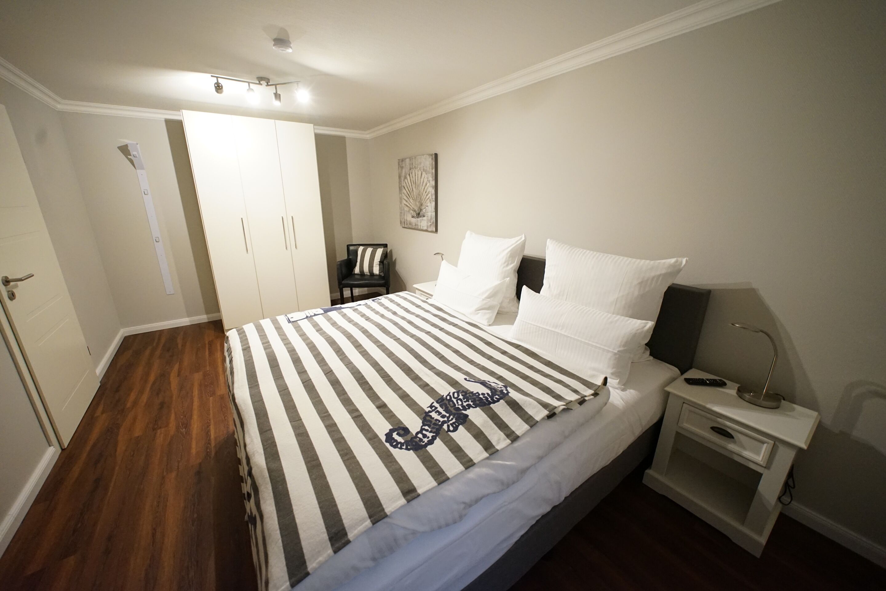 Een slaapkamer met een bed, nachtkastje, stoel en deur.