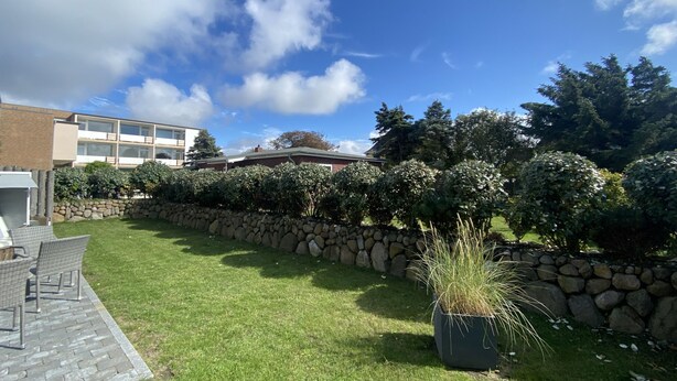 Ein gepflegter Garten mit Steinmauer, Rasen und einer Sitzgelegenheit mit Korbmöbeln.