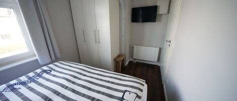 A bedroom with a bed, a wardrobe, a television mounted on the wall, and a window with curtains.