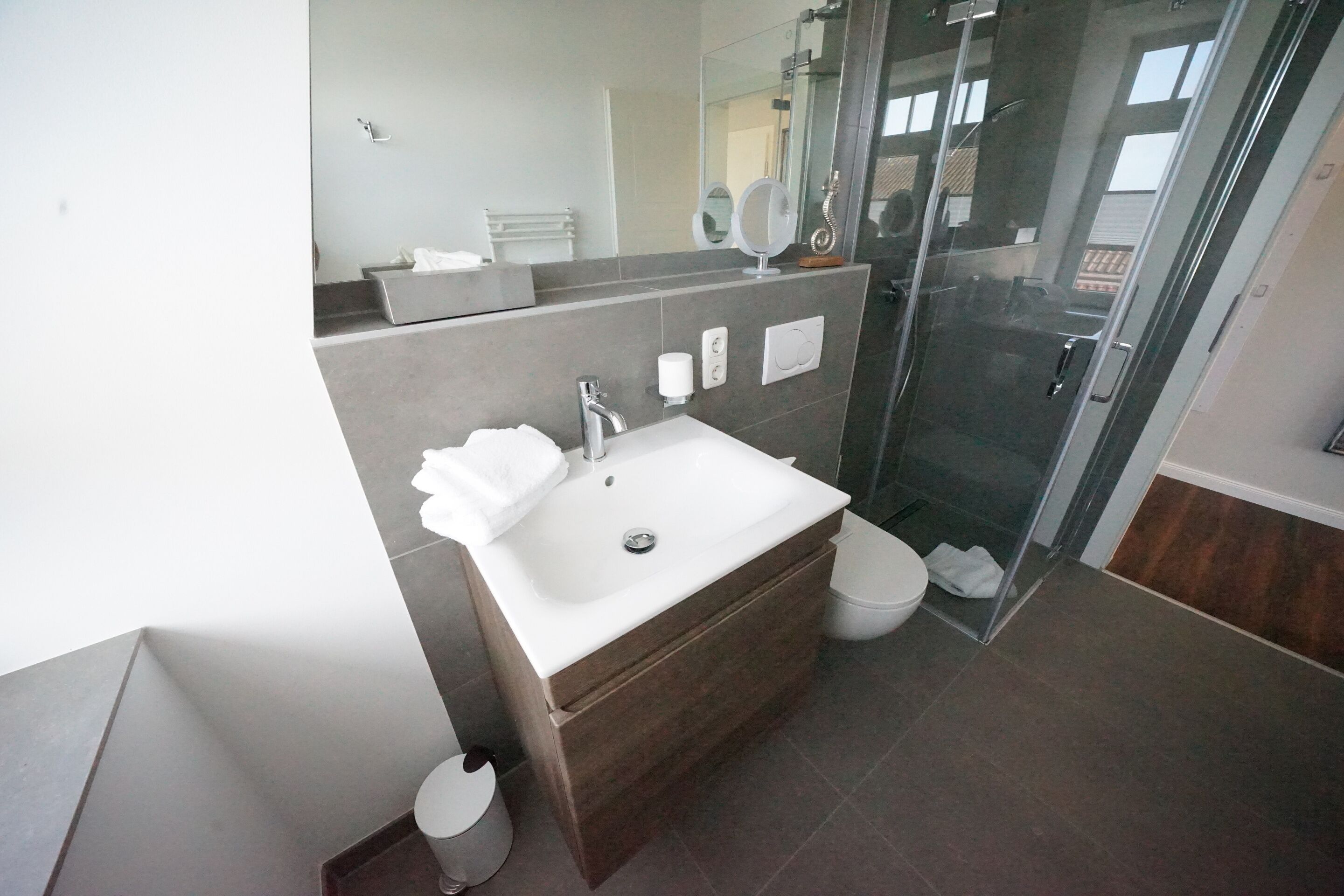 Un baño moderno con lavamanos blanco, espejo y cabina de ducha de vidrio.