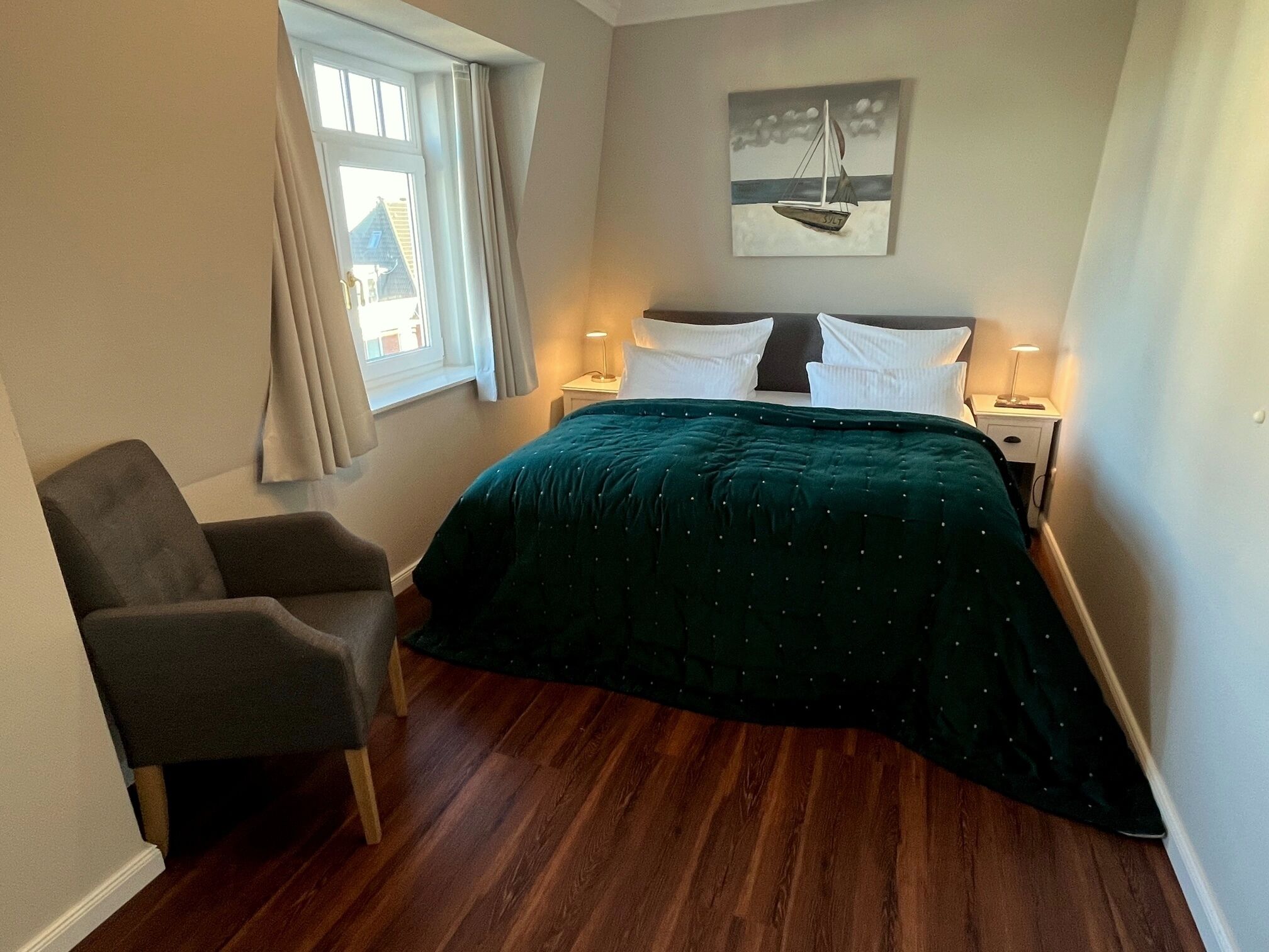 A bedroom with a bed, a chair, a nightstand, a lamp, and a painting on the wall.