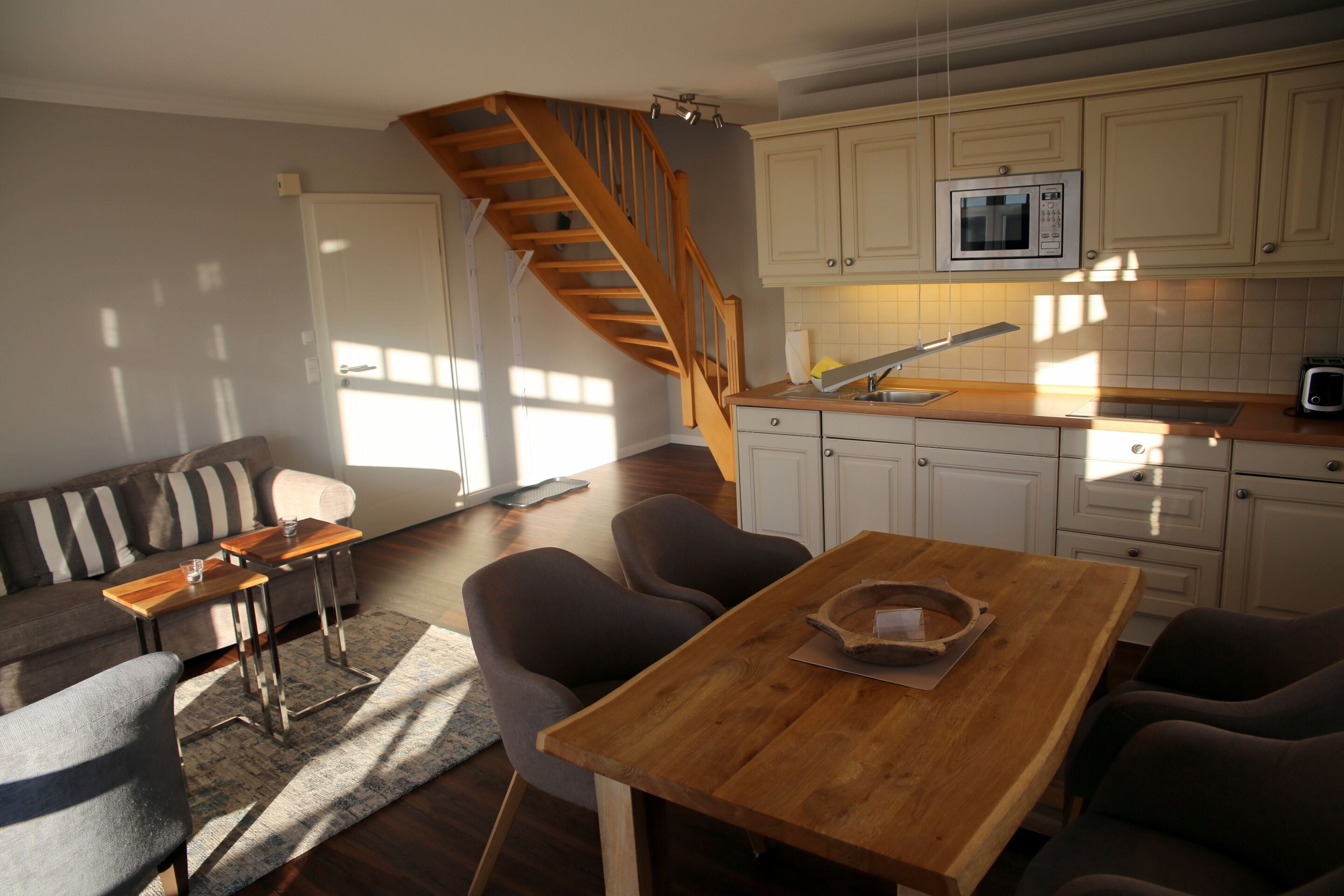 Eine moderne Küche mit Holztisch und -stühlen, einer eingebauten Mikrowelle und einer Treppe, die zu einer weiteren Ebene führt.