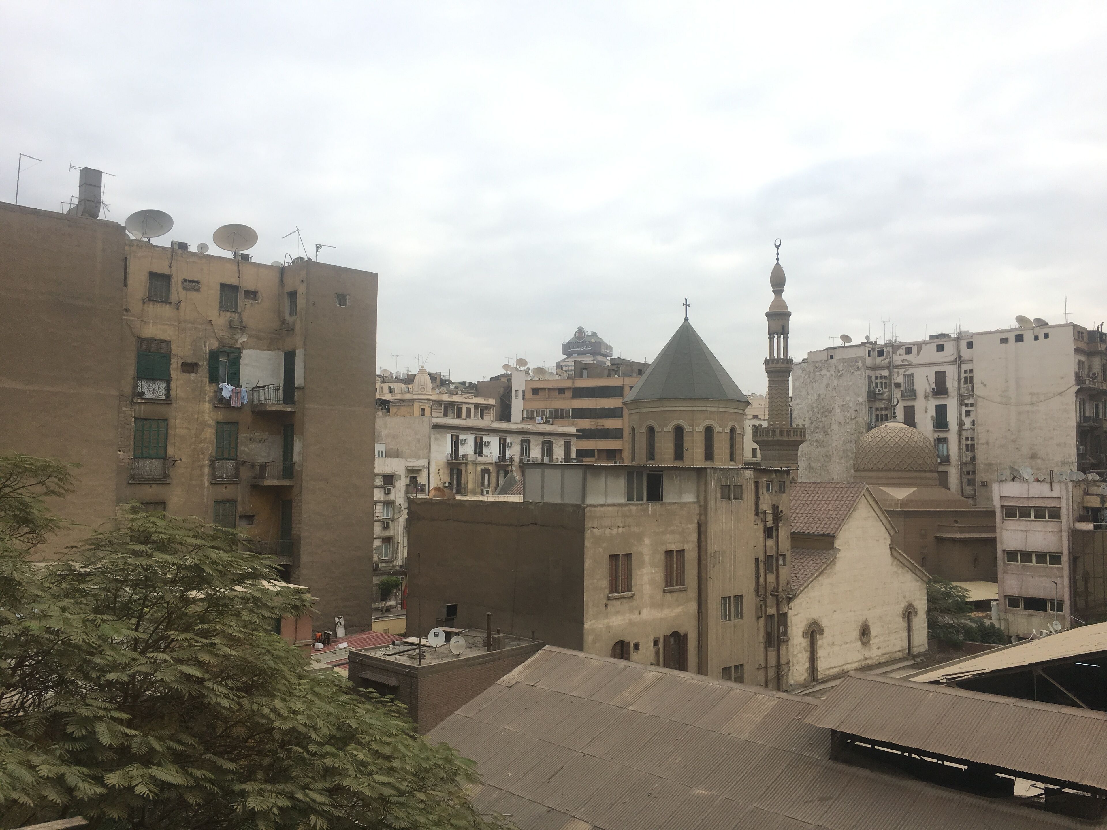 A view of a cityscape with a prominent mosque featuring a dome and minaret, surrounded by residential buildings with satellite dishes.
