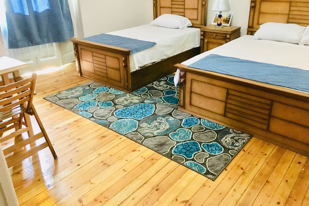 Habitación de hotel con dos camas, piso de madera, alfombra estampada y escritorio con silla.