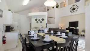 Un espacio habitable amplio con una mesa de comedor para cuatro, un sofá, un televisor y una cocina con refrigerador y armarios.