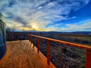 A wooden deck with a metal railing overlooking a landscape with mountains and a cloudy sky. - Monte Cristo YURT Adventure (Hyrum)