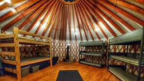 Una yurt con letti a castello in legno, un forno a stufa per riscaldamento centralizzato e un parete a griglia.