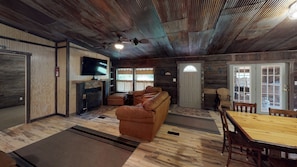 Un interior rústico con un sofá, televisor, chimenea y comedor.