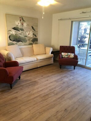Un salon avec un canapé à rayures, un fauteuil rouge et un grand tableau représentant des fleurs de lotus au mur.