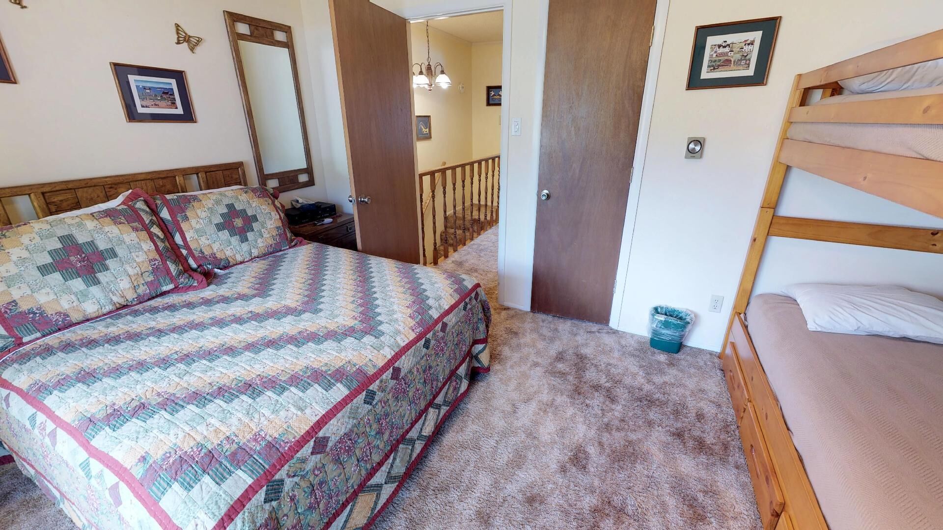 Une chambre avec un grand lit, un lit plus petit, une tête de lit en bois, un miroir et un escalier menant à une autre pièce.