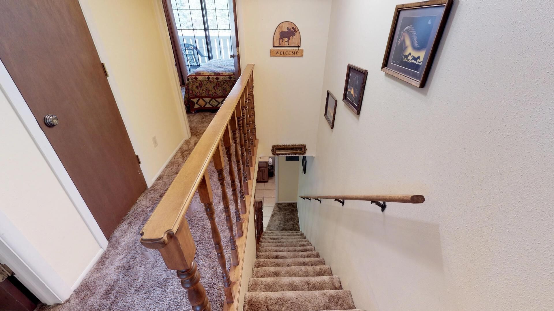 A wooden staircase with a handrail, carpeted steps, a welcome sign, and framed pictures on the walls.