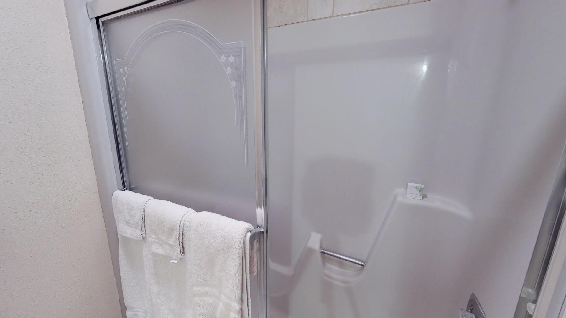 A bathroom with a glass shower door, a white towel hanging on the door, and a small white object on the floor.