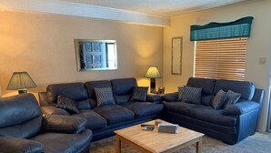Ein Wohnzimmer mit zwei dunkelbraunen Ledersofas, einem Holztisch, einer Lampe und einem Fenster mit Jalousien.