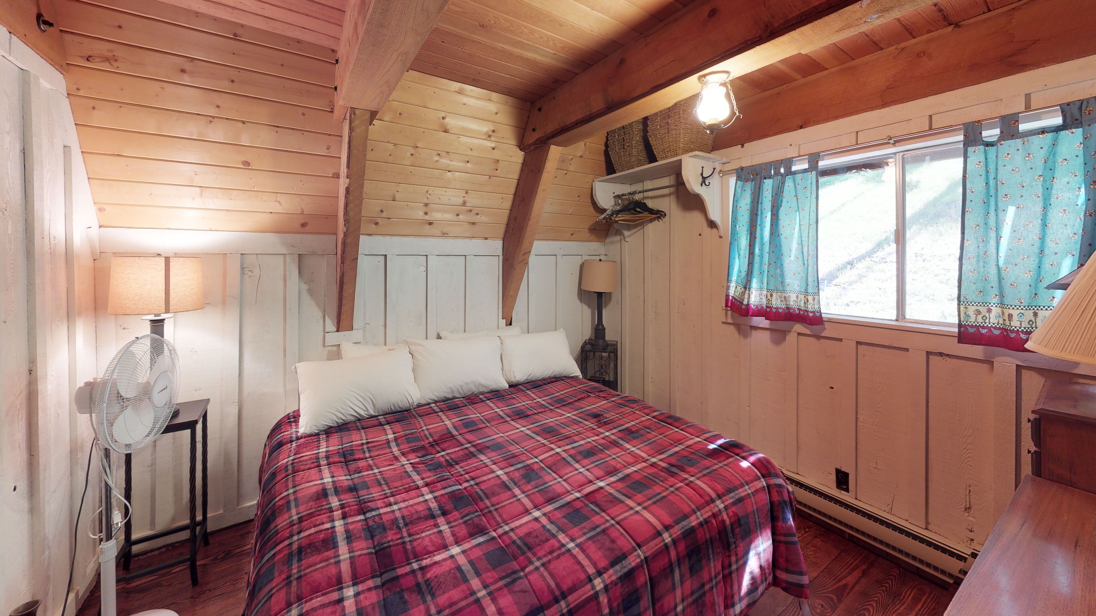 A cozy room with a bed, two wall-mounted lamps, a window with curtains, and a wooden ceiling.