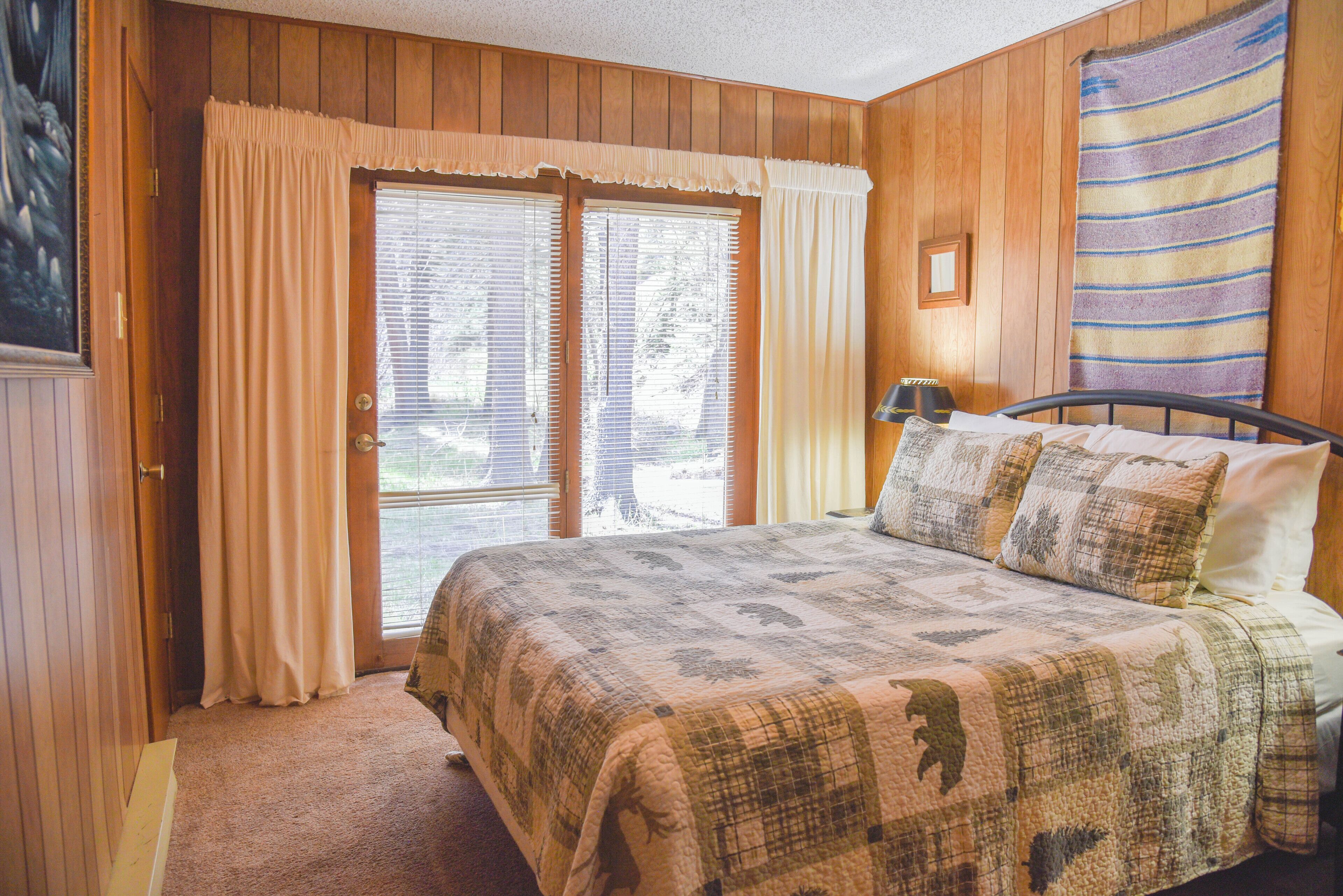 Ein Schlafzimmer mit einem großen Bett, Holzwänden, einem Fenster mit Vorhängen und einer Decke auf dem Bett.