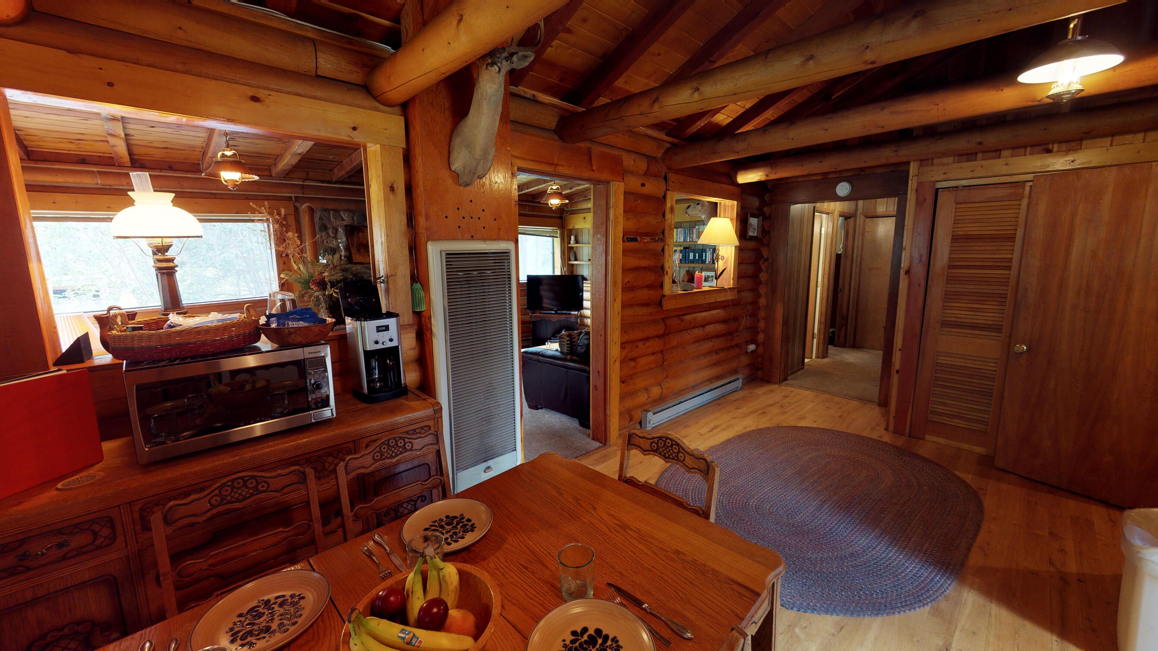 Interior de uma cabana de madeira com uma mesa de jantar posta para dois, uma cafeteira, micro-ondas e uma televisão ao fundo.