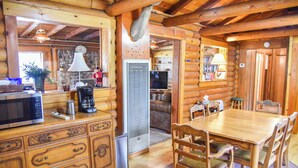 A wooden cabin interior with a dining area, kitchen, and living space.