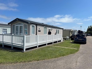 A mobile home with a porch and a fenced yard. - 3 Bed Static caravan 12ftx38ft nr. beach & pool. New adventure land wrap decking (Caister-on-Sea)