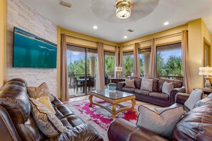 A spacious living room with a leather sofa, a coffee table, and a TV mounted on a brick wall.