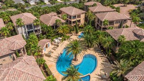 A resort with multiple buildings, a central swimming pool, and surrounding palm trees.