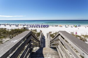 Un escalier en bois mène à une plage où se trouvent des parasols et des chaises de plage.