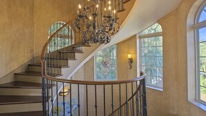 A grand spiral staircase with a wrought iron railing and a decorative chandelier.