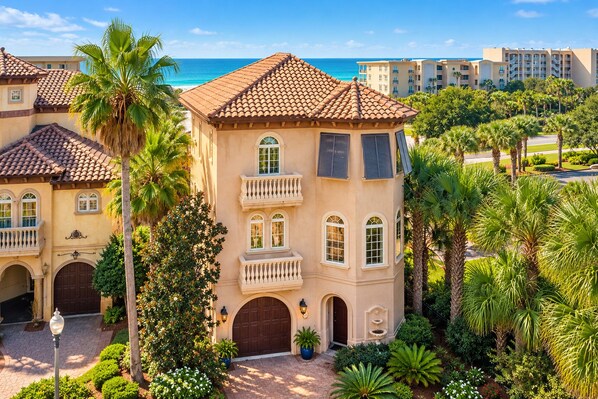 A multi-story building with a tiled roof, multiple balconies, and a courtyard with palm trees.