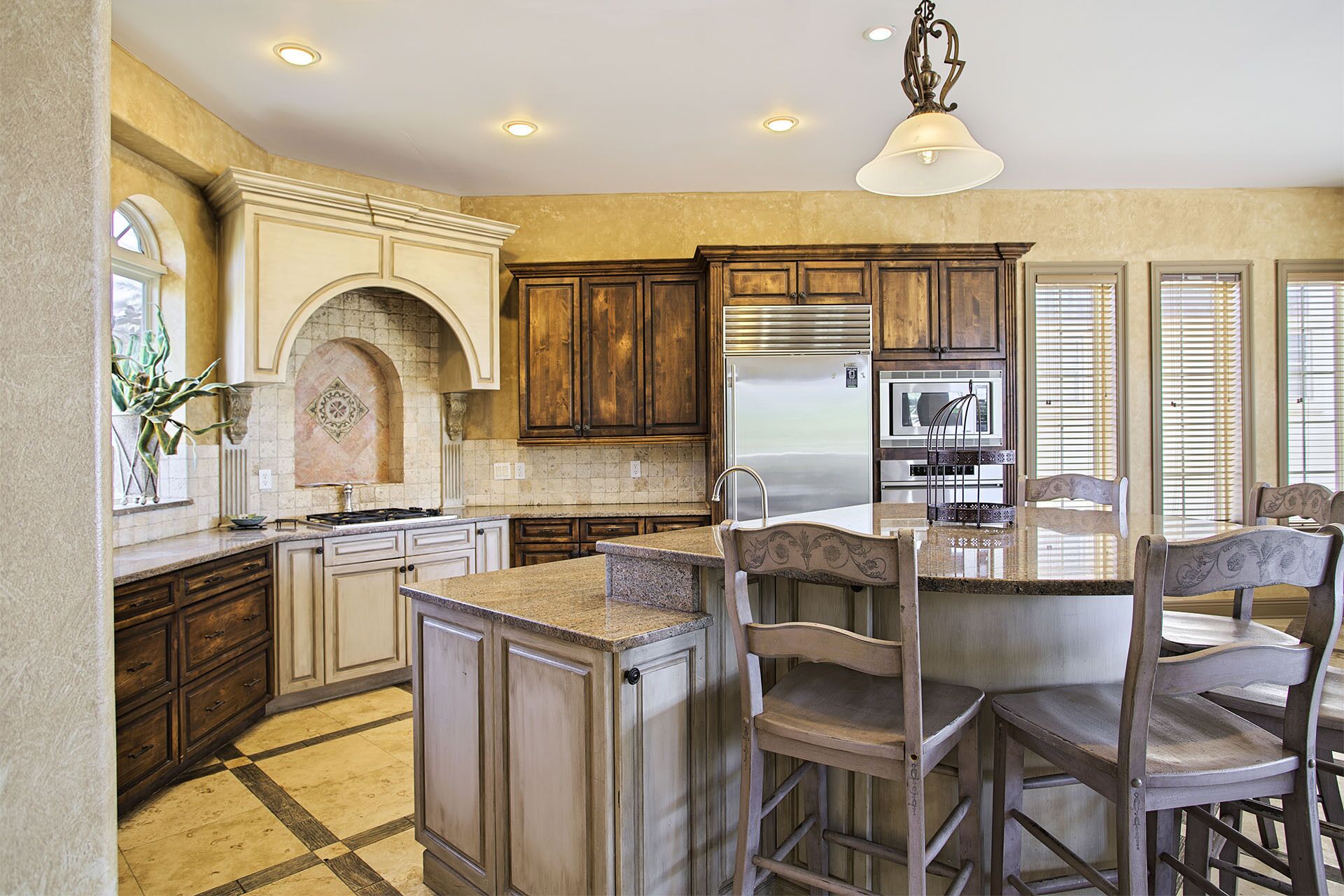 A kitchen with a central island, wooden cabinets, a stainless steel refrigerator, and a chandelier.