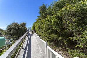 A wooden pathway leading to a metal gate, surrounded by dense greenery. - Galileo - Gated Subdivision, Gulf Views, Community Pool + Hot Tub, Pet Friendly! (Miramar Beach)
