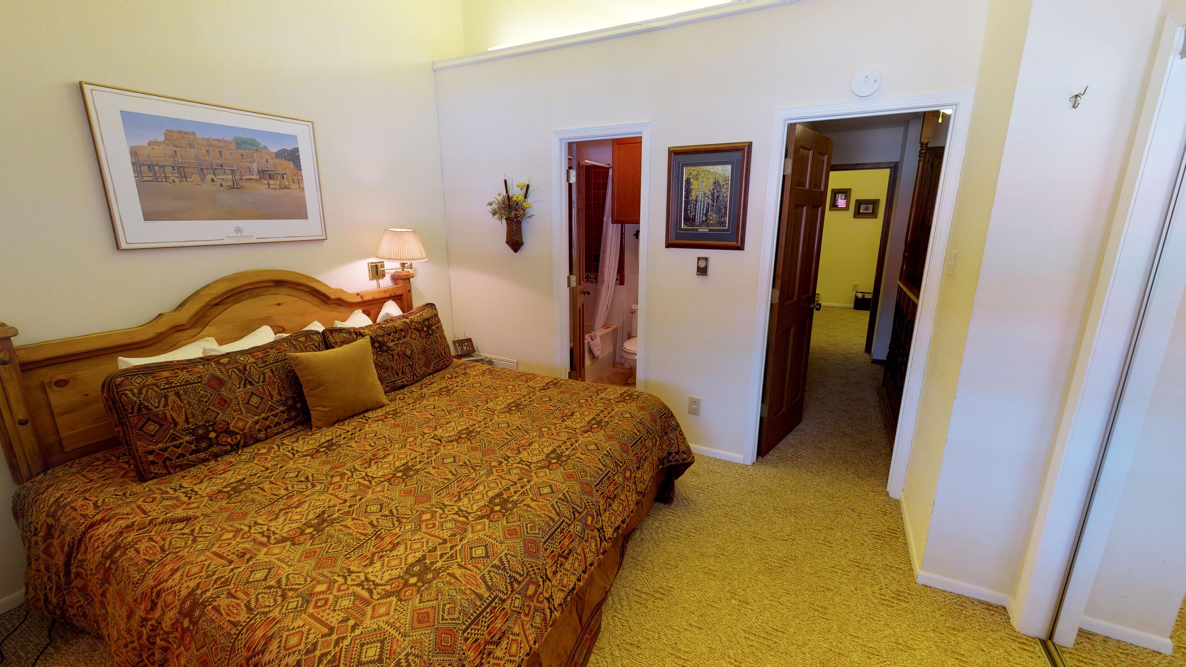 A bedroom with a large bed, a nightstand, a lamp, and a framed picture on the wall.