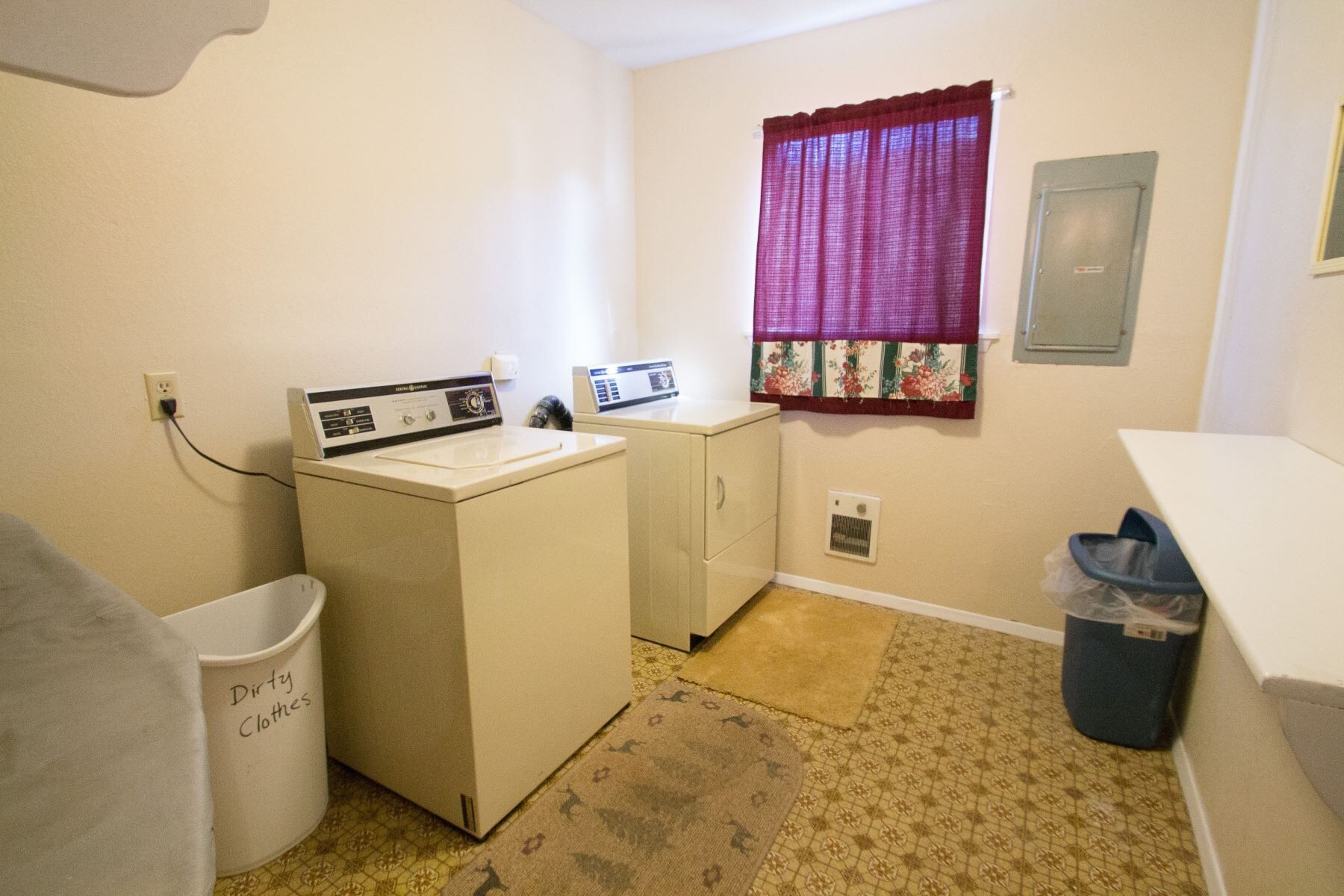 A laundry room with a washing machine, dryer, and a trash bin labeled "Dirty Clothes".