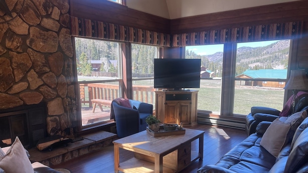 A cozy living room with a stone fireplace, leather sofas, a wooden coffee table, and a television on a cabinet. - Valley View in the Upper Valley (Red River)