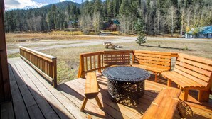 A wooden deck with a round table and benches, overlooking a forested area with a cabin in the background. - Valley View in the Upper Valley (Red River)
