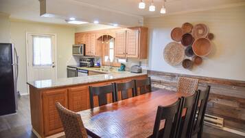 A kitchen with wooden cabinets, a central island with chairs, a microwave, and a sink.