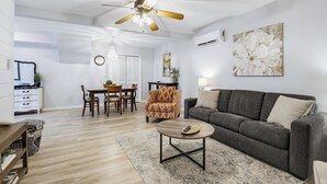 Un amplio salón con un sofá gris, una mesa de centro y un comedor con muebles de madera.