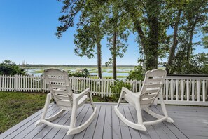 Deux fauteuils à bascule sur une terrasse en bois, avec une clôture blanche et une vue sur un lac et des arbres.