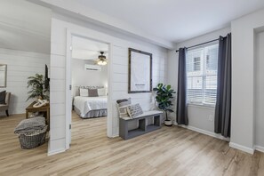 Una sala moderna con piso de madera, un banco, una planta en maceta, una cama con cabecera y un mapa enmarcado en la pared.