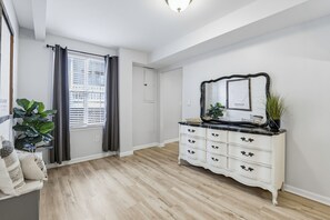 Una habitación con un aparador blanco, un espejo grande, una planta en maceta y una ventana con cortinas.