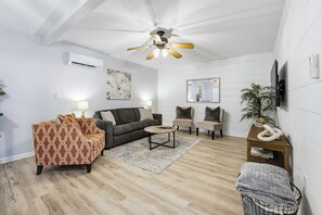 Een moderne woonkamer met plafondventilator, bank, salontafel en televisie.