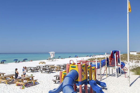 Une plage équipée de tables de pique-nique, d’une tour de surveillance pour les sauveteurs et d’aires de jeux pour enfants.