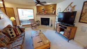 A living room with a fireplace, a television, a wooden coffee table, and a patterned sofa.