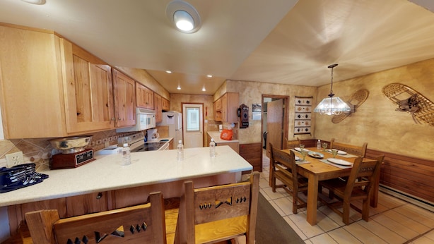 A kitchen with wooden cabinets, a central island, and a dining area with wooden chairs and a table.