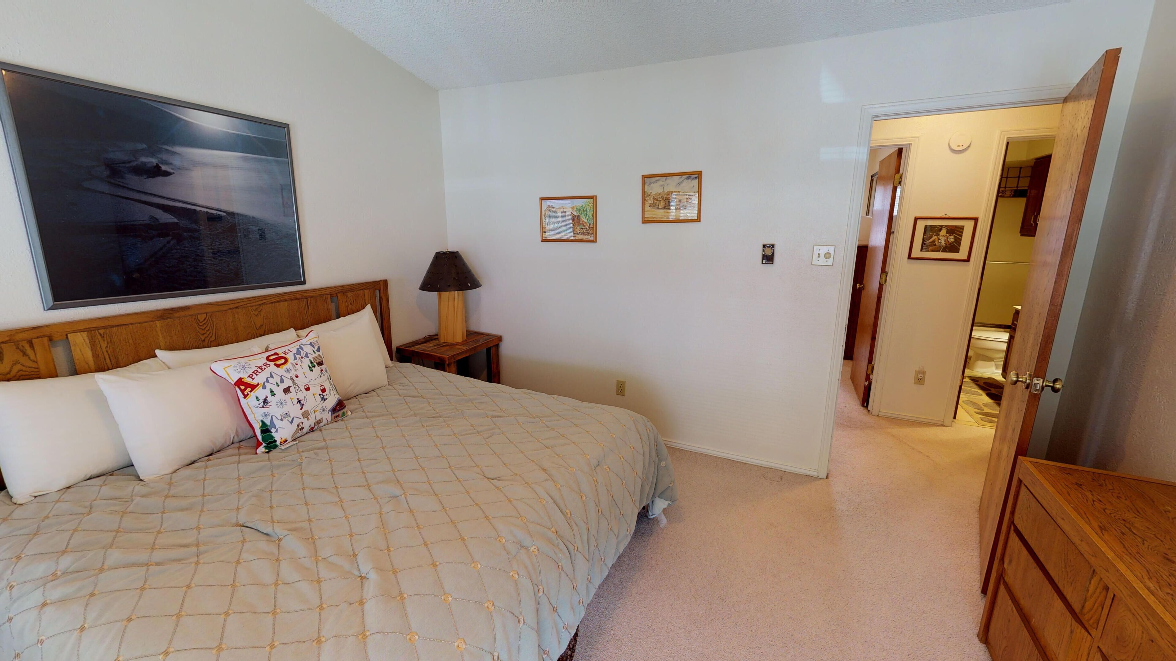 A bedroom with a bed, a nightstand, a lamp, and a door leading to another room.