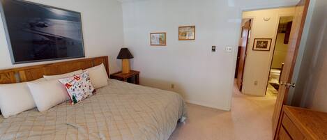A bedroom with a bed, a nightstand, a lamp, and a door leading to another room.
